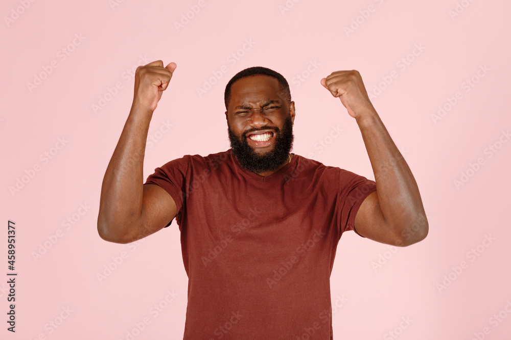 Excited young Afro-American man with stylish beard happy of big win poses for camera on pink background in studio close view Excited young Afro-American man with stylish beard happy of big win poses for camera on pink background in studio close view