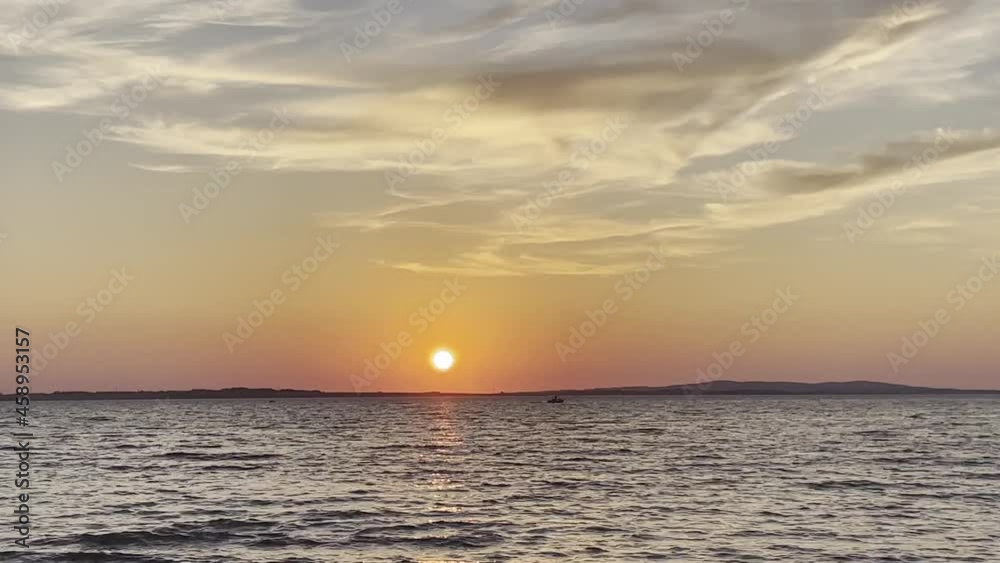 Orange sun over wavy waters during summer sunset and small boat passing Orange sun over wavy waters during summer sunset and small boat passing