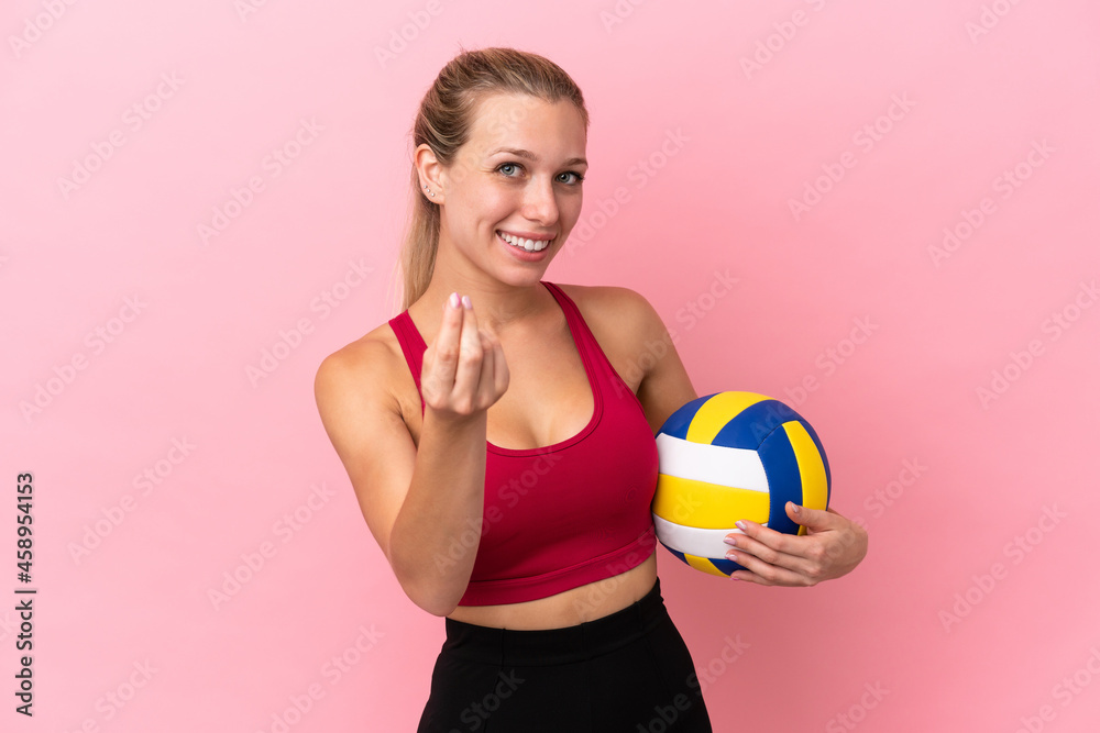 Young caucasian woman playing volleyball isolated on pink background making money gesture
