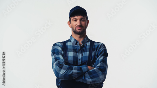 Workman in cap and overalls standing with crossed arms isolated on white