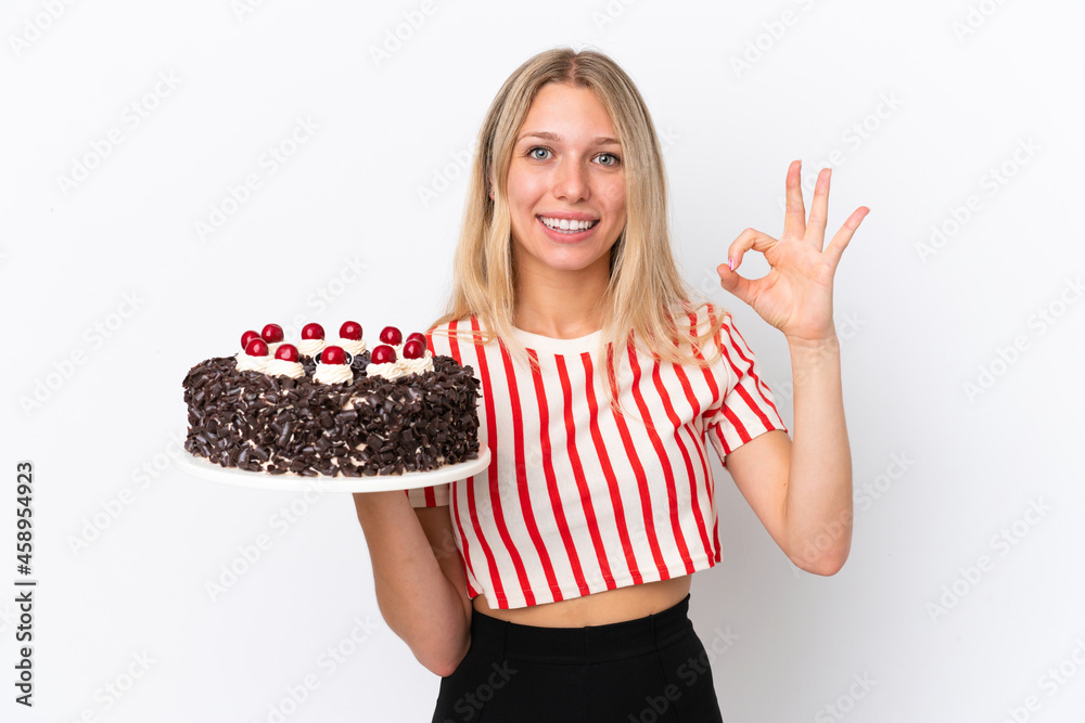 Young caucasian woman holding birthday cake isolated on white background showing ok sign with fingers Young caucasian woman holding birthday cake isolated on white background showing ok sign with fingers