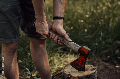 hand holding axe in the stump. a man is chopping wood