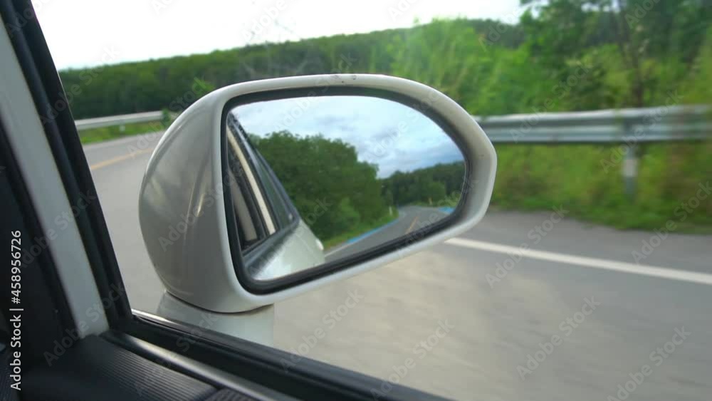 Slow motion of driving car view in side with mirror wing of white car. Looking towards the curving asphalt road and green grass view. Slow motion of driving car view in side with mirror wing of white car. Looking towards the curving asphalt road and green grass view.
