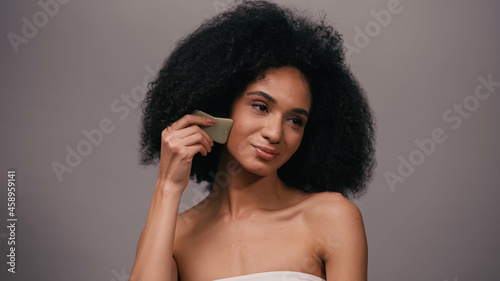 african american woman with bare shoulders using jade gua sha stone isolated on grey