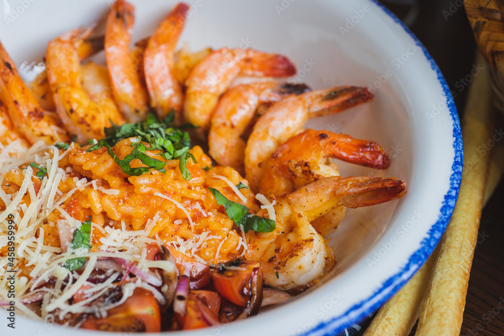 Traditional bright shrimp risotto in a bowl on a table in a restaurant with a beautiful decor in a dark key close-up.