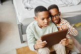 High angle view at two teenage African-American boys using digital tablet together while siting on floor in cozy room, copy space