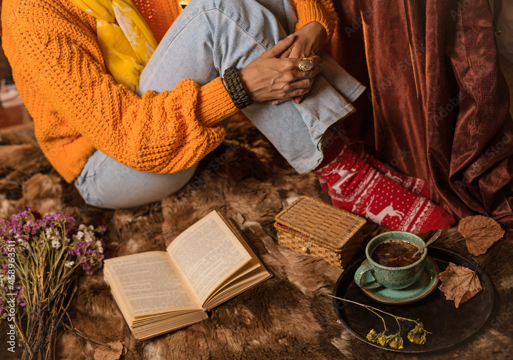 Beautiful woman in orange sweater reading a book and enjoying her coffee Beautiful woman in orange sweater reading a book and enjoying her coffee