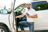 Man engineer builder wearing a white hard hat, shirt in front of his pickup using cellphone