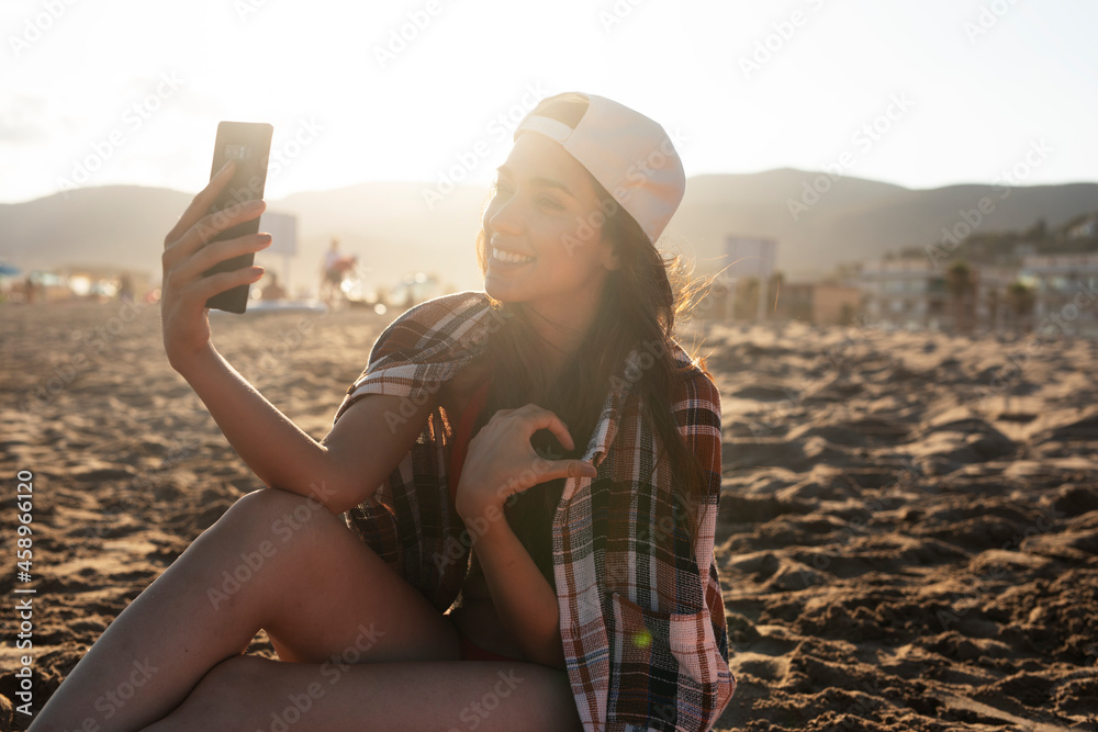 Portrait of beautiful female surfer with her surfboard. Young woman using the phone while relaxing on the beach...