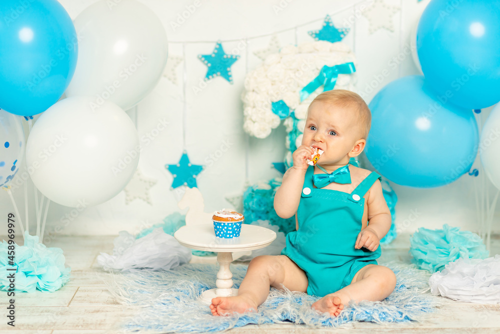 baby eats birthday cake and celebrates first birthday in photo zone in blue color with balloons and cake