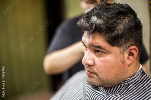 Young barber making haircut of bearded man in barbershop
