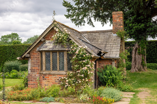 Very old small red brick garden house with slate roof, mullioned windows and pink climbing rose. photo