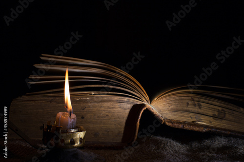 A candle burns next to an open old book. the concept of secret knowledge and mysticism. Selective focus on a candle flame. photo