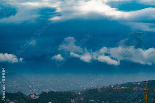Dense rain clouds over the city and the mountains on a rainy summer morning, in the foreground in the right corner is the jet of a construction crane