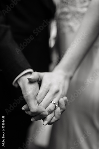 Black and White photo Bride and groom holding hands with woman's hand on man's hand with wedding rings close up bride and groom holding hands close up photo