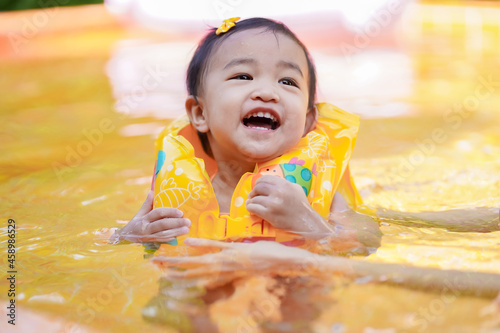 Asian cute baby girl in a life vest holding by her mother enjoying in the swimming pool.
