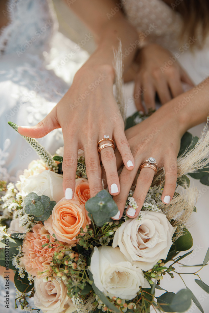 Beautiful aesthetic same-sex wedding two brides lesbian hold hands with wedding  rings and bouquet with orange and white roses close up on a sunny day Stock  Photo | Adobe Stock