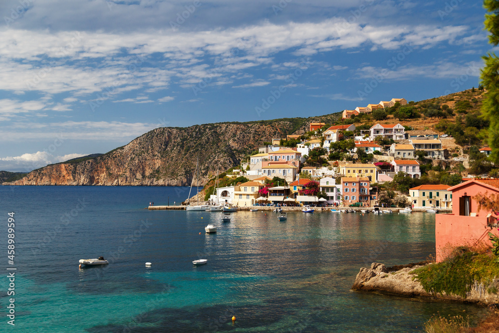 A view at blue bay, sea-front street of Asos village, greek colorful houses and turquoise Ionian Sea water. Luxury summer vacation and holiday at Cephalonia island. Greek island travel background.