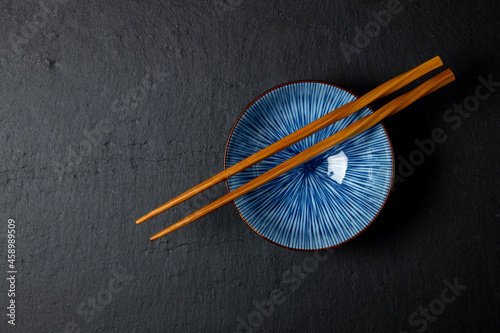 Blue bowl with wooden chopsticks on a black plate