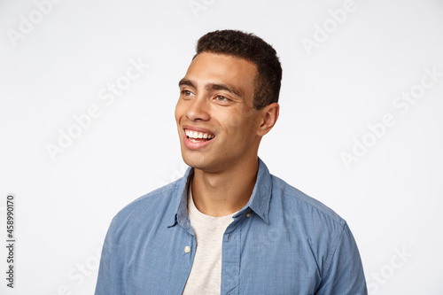 Close-up portrait enthusiastic, handsome brazilian man, look amused and entertained left, smiling happy, contemplate interesting promo, have joyful conversation, standing amazed white background