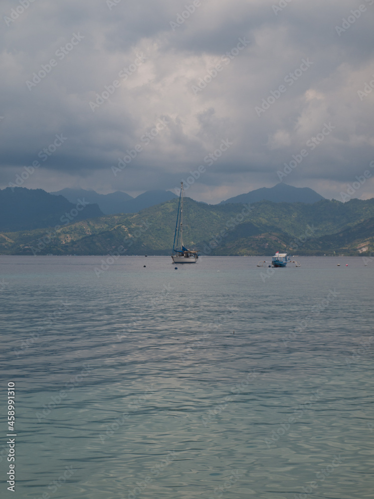 Tropical sea with sailboats with Lombok island in background and cloudy sky