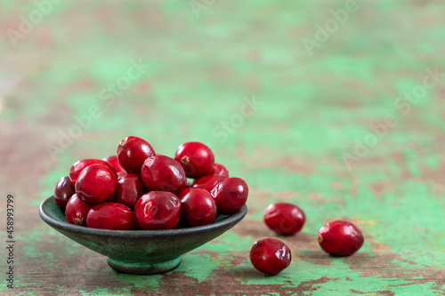 Fresh cranberries fruits in rustic asian bowl on old green wooden background and daylight.