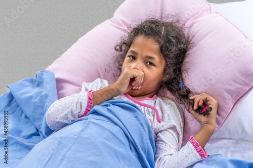 Fotografija Close portrate cute multiracial girl of 6-10 years old is sucking his thumb in the bed