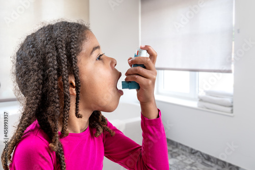 Close-up portrait of cute 5 year old girl using his asthma inhaler, profile view white background. photo