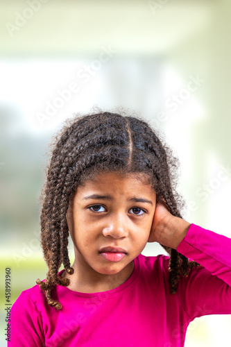 Little african-american girl with hearing problem on light background, suspicion of otitis.
