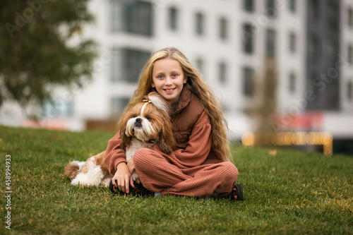 Portrait of beautiful preteen girl petting and hugging shih tzu dog outdoors.