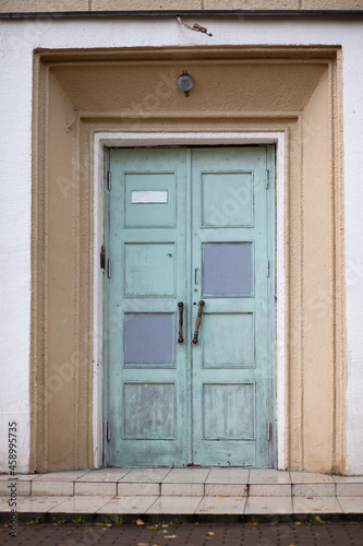 An old wooden blue shabby door to the entrance of a multi-storey residential building.