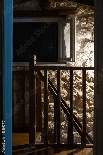 Dark second floor interior in traditional Mediterranean house. Opened doorway with stairs railings and window in night lamp light