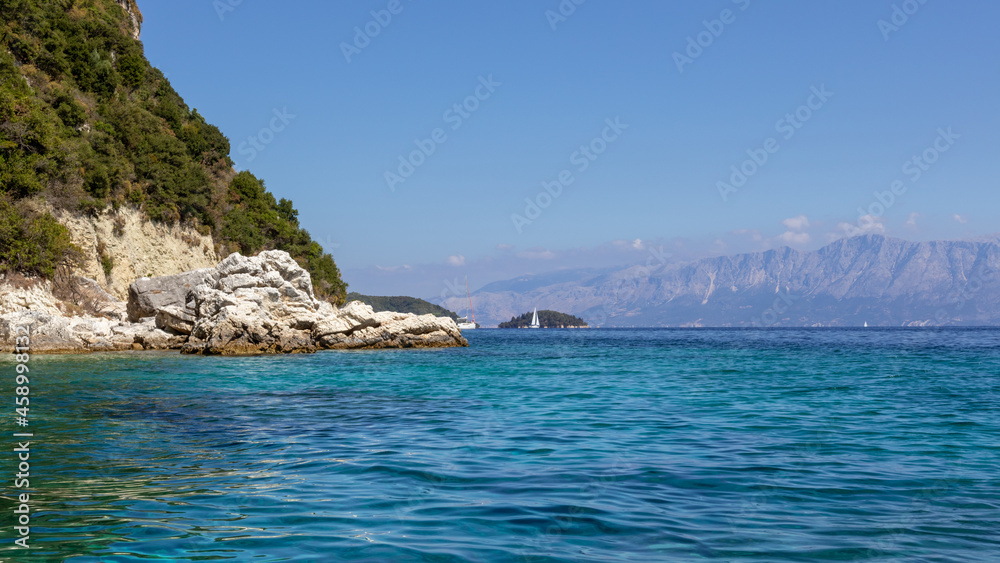 Scenic rocks in blue rippled vivid clear water of Ionian Sea with cliffs and bright sky. Nature of Lefkada island in Greece. Summer vacation travel destination