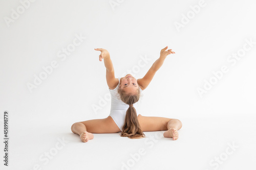 slim artistic teenager girl in white leotard trains on white background in rhythmic gymnastic exercise, children's professional sports photo