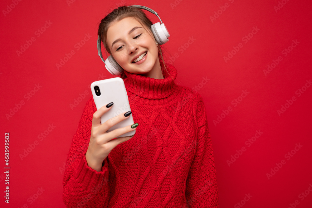 Photo of beautiful joyful smiling young woman wearing stylish casual clothes isolated over background wall holding and using mobile phone wearing white bluetooth headphones listening to music and Photo of beautiful joyful smiling young woman wearing stylish casual clothes isolated over background wall holding and using mobile phone wearing white bluetooth headphones listening to music and