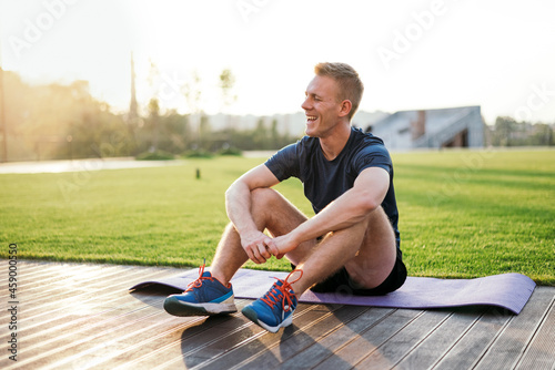 Fototapeta Naklejka Na Ścianę i Meble -  athletic sportsman resting after sport in the park and looking far away at the sunset and smiling