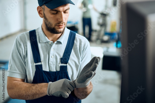 Auto mechanic uses protective gloves while working at repair shop.