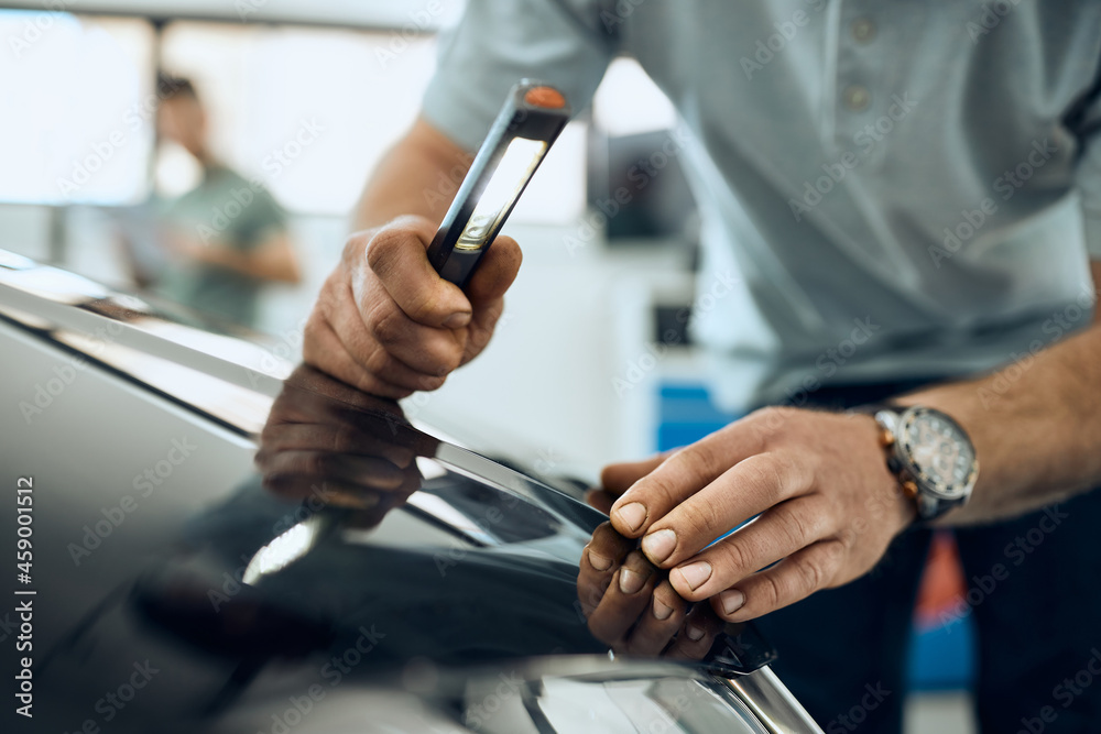 Close-up of car mechanic examines vehicle hood with lamp at workshop. Close-up of car mechanic examines vehicle hood with lamp at workshop.