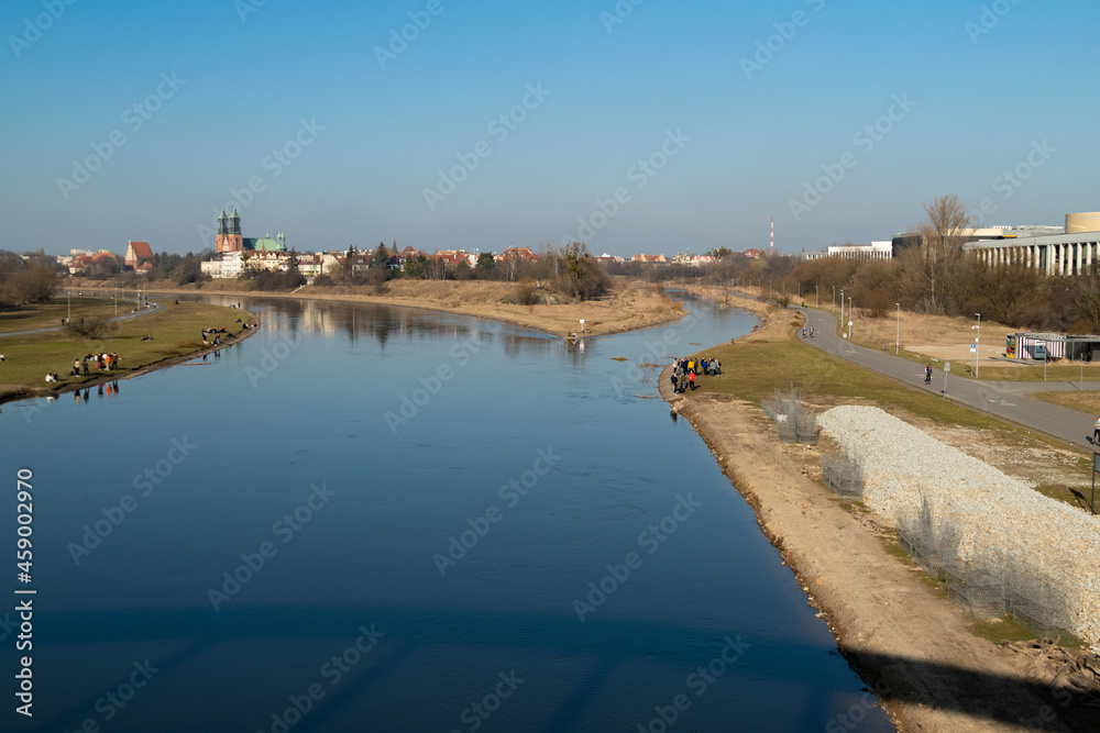 The fork of the Warta river in spring with young people resting by it on a sunny day