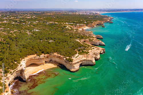 Aerial view of a boat, catamaran and a yacht cruising along the sea near the cliffs of Praia da Corredoura beach in Lagoa, Algarve, Portugal. photo