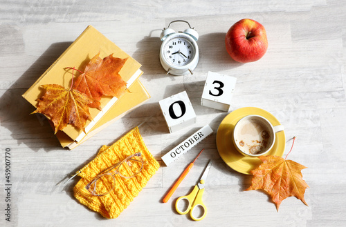 Calendar for October 3 : name of the month in English, cubes with numbers 0 and 3, books, alarm clock, maple leaves, red apple, knitted scarf, cup of coffee, eyeglasses on a gray background