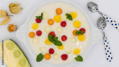 Cold melon cream with pieces of melon, raspberries, mango, physalis peruviana and mint leaves on a white background.