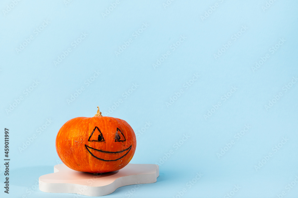 Small orange carved pumpkin on blue background with copy space. Concept celebration of Halloween or Thanksgiving. Cosmetics podium for halloween. Autumn still life. Small orange carved pumpkin on blue background with copy space. Concept celebration of Halloween or Thanksgiving. Cosmetics podium for halloween. Autumn still life.