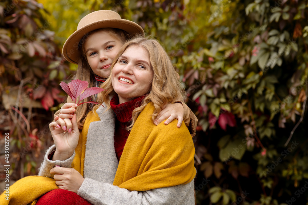 Fototapeta premium A young adult blonde mother with a 7-year-old daughter on a walk in the autumn park hug and laugh 