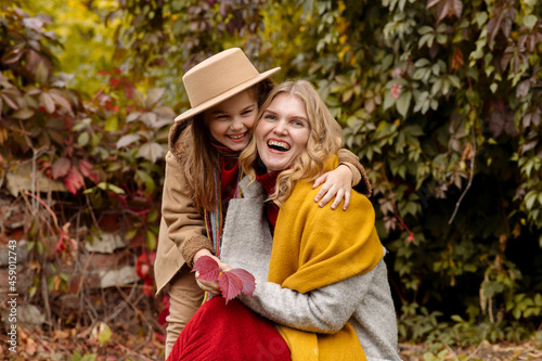 A young adult blonde mother with a 7-year-old daughter on a walk in the autumn park hug and laugh 
