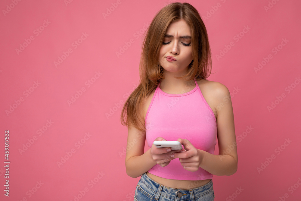 closeup Photo shot of attractive thoughtful thinking upset good looking young woman wearing casual stylish outfit poising isolated on background with empty space holding in hand and using mobile phone