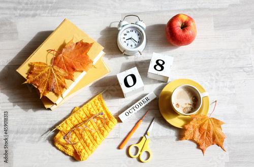 Calendar for October 8 : name of the month in English, cubes with numbers 0 and 8, books, alarm clock, maple leaves, red apple, knitted scarf, cup of coffee, eyeglasses on a gray background