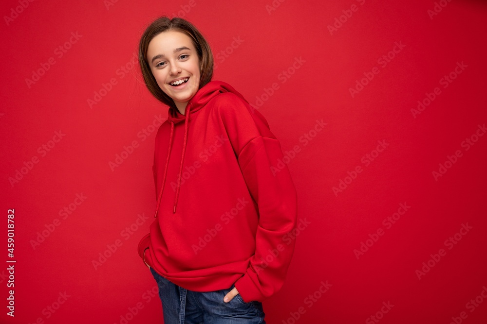 Fototapeta premium Shot of beautiful happy cool smiling brunette little girl wearing trendy red hoodie standing isolated over red background wall looking at camera