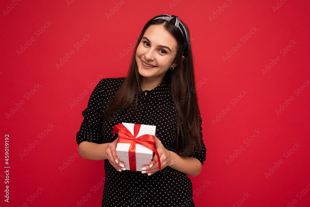Beautiful happy brunette girl isolated over colourful background wall wearing stylish casual clothes holding gift box and looking at camera Beautiful happy brunette girl isolated over colourful background wall wearing stylish casual clothes holding gift box and looking at camera