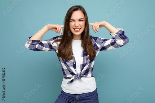 Don't want to hear it! Young emotional positive attractive brunette female person isolated on blue background with copy space and covering ears